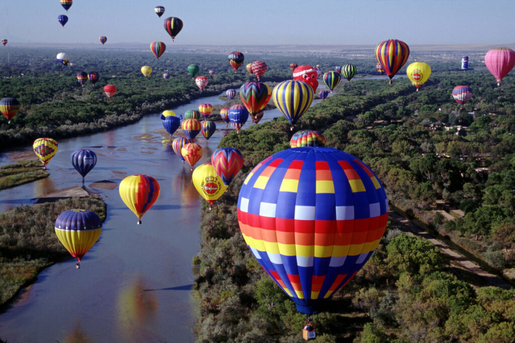 Hundreds of brightly colored balloons floating over the Rio Grande River by Ron Behrmann