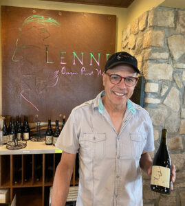 Lenne Estate Winery owner, Steve Lutz with a Lenne Logo in the background and holding a bottle of his wine