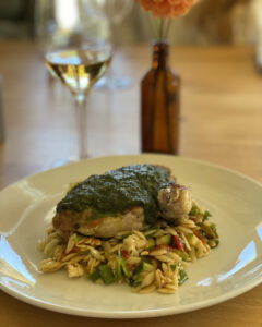Halibut smothered in pesto sauce on top of a Greek orzo salad