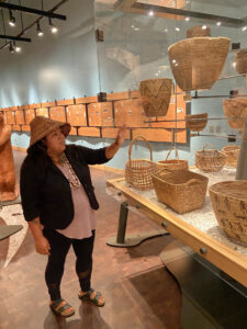 Tribal Leader, Danita Holmes, describes the baskets at the Suquamish Museum while wearing a woven hat to ward off rain