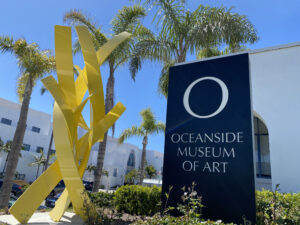 Bright yellow metal sculpture of twisting vines called Offshore by Matt Devine next to the Oceanside Museum of Art